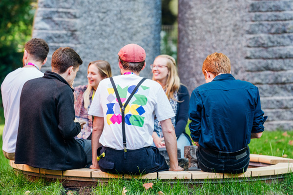 Menschen sitzen draußen im kreis auf einer Holzbank