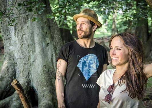 Männlich gelesene Person und weiblich gelesene Person in modischen T-Shirts vor einem Baum