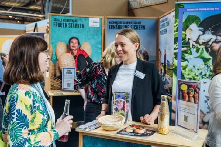 Zwei weiblich gelesene Personen sprechen miteinander am Oikocredit Stand auf dem GLS Jubilaeumsfestival