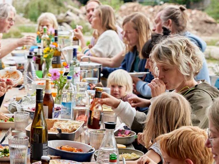 Viele Menschen essen zusammen draußen im Garten an einer langen Tafel.